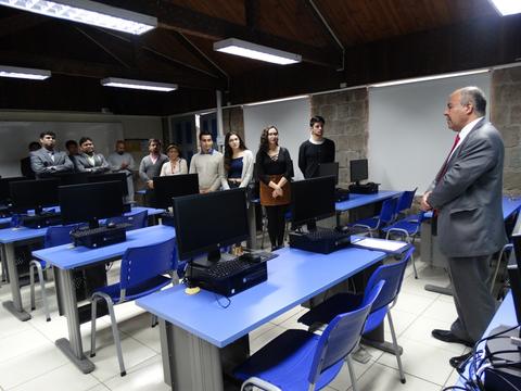 Un grupo de personas escucha a un hombre que habla frente a varias computadoras en un aula.