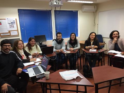 Un grupo de personas sonrientes se encuentra en un aula, rodeados de computadoras y material de trabajo.
