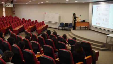Una presentación en un auditorio lleno de asientos rojos con una ponente frente a una pantalla.