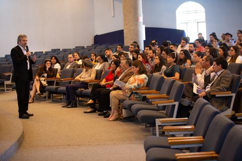 Un orador habla frente a una audiencia en un auditorio.