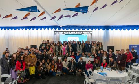 Un gran grupo de personas posando juntas en un evento bajo un techo decorado con banderines.