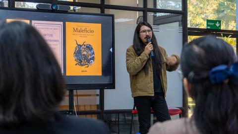 Un presentador habla sobre un libro titulado 'Maleficio' frente a una audiencia.