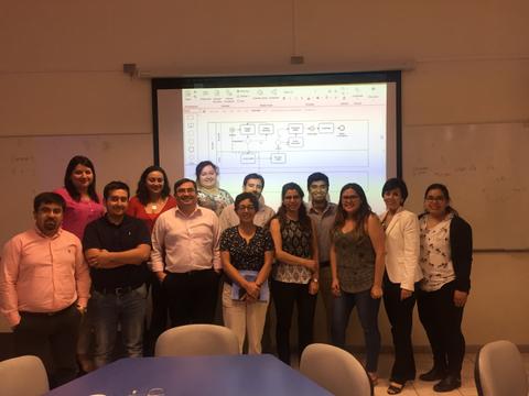 Un grupo de personas posando frente a una pantalla con un diagrama en un ambiente de trabajo.