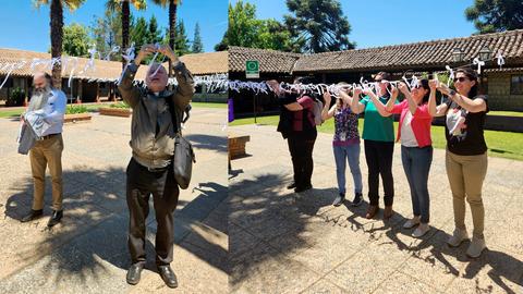 Un grupo de personas sostiene una cadena de figuras recortadas en papel en un espacio al aire libre.