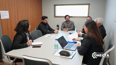 Un grupo de seis personas se reúne en una sala de conferencias con una mesa de trabajo y una laptop.