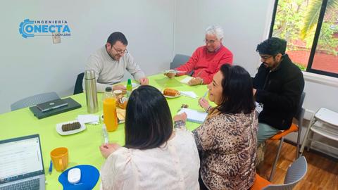 Un grupo de personas discutiendo en una reunión alrededor de una mesa con comida y bebidas.