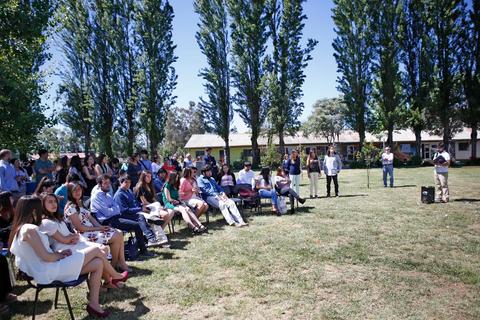 Un grupo de personas escuchando a un orador en un evento al aire libre rodeado de árboles.
