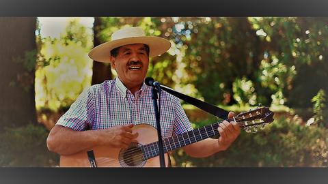 Un hombre con sombrero toca la guitarra mientras sonríe al aire libre.