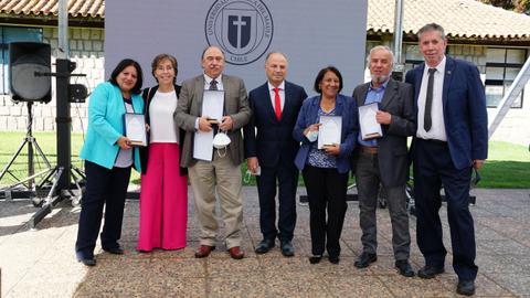 Un grupo de siete personas sonríen mientras sostienen reconocimientos en una ceremonia al aire libre.