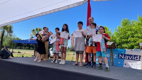 Un grupo de niños y adultos posan en un escenario al aire libre sosteniendo certificados de reconocimiento.