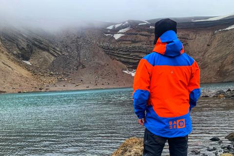 Una persona contempla un paisaje montañoso y un lago de aguas turquesas en un ambiente nublado.