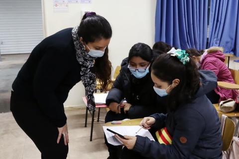 Una maestra ayuda a sus estudiantes que están sentados en un aula mientras utilizan una tableta.
