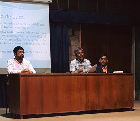 Tres hombres discuten sobre ética en una presentación académica.