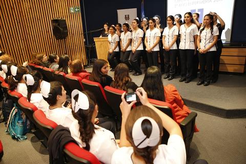 Un grupo de estudiantes se presenta en un evento frente a una audiencia sentada.