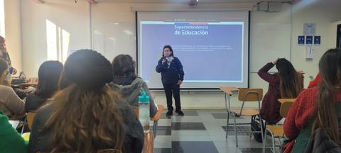 Una persona habla frente a un grupo en un aula con una presentación en la pantalla.