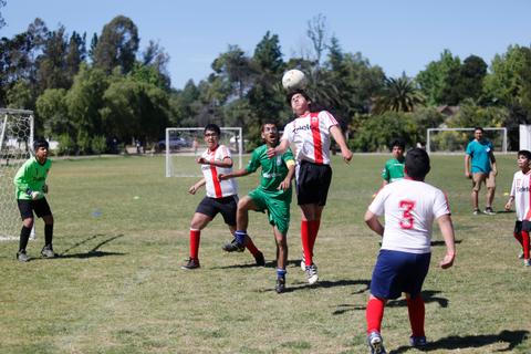Un grupo de jóvenes juega al fútbol en un campo al aire libre bajo un cielo soleado.
