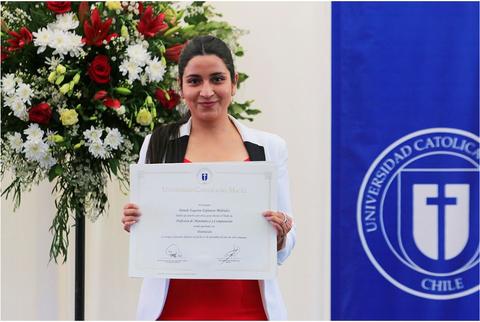 Una mujer sostiene un certificado de graduación frente a una decoración floral.