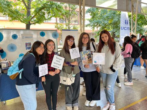 Un grupo de cinco estudiantes sonríe mientras sostienen carteles en un evento escolar.