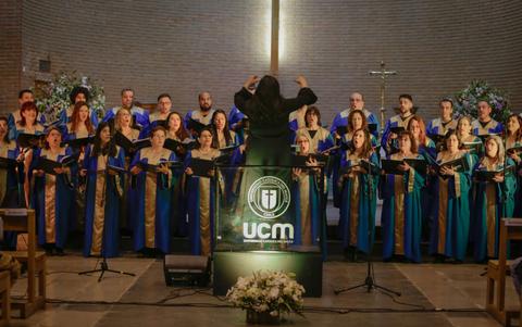 Un coro con muchos cantantes vestidos con túnicas azul y dorada están actuando en un escenario interior.