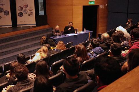 Una conferencia con un orador y una audiencia escuchando en un auditorio.