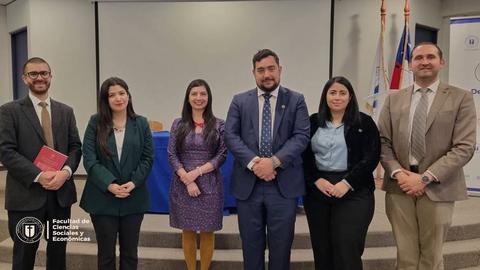 Un grupo de seis personas vestidas formalmente posan en un recinto académico.