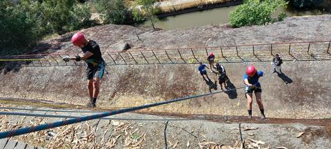 Un grupo de personas practica rappel en una ladera junto a un río.