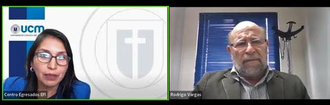 Una reunión virtual entre dos personas, una mujer con gafas y un hombre con barba, en un fondo institucional.