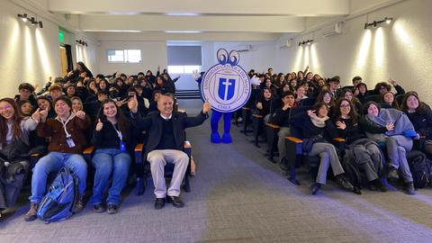 Una multitud de estudiantes felices posando en un auditorio con un personaje mascota.