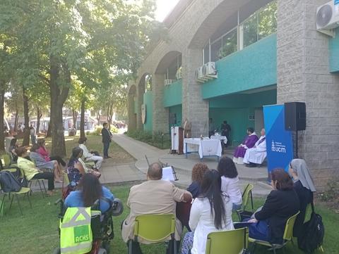 Un evento al aire libre con un grupo de personas sentadas frente a una mesa en un espacio verde.