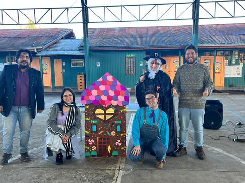 Grupo de personas posando junto a una casa de cartón decorada en un evento escolar.