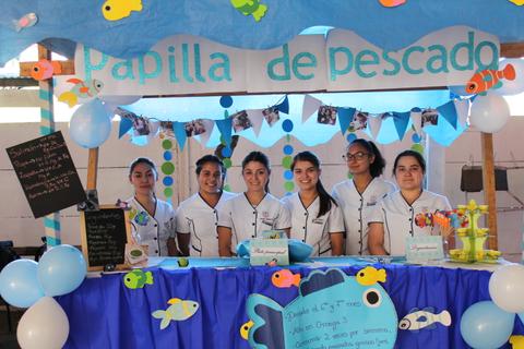 Un grupo de seis jóvenes sonríe detrás de un colorido puesto llamado 'Papilla de pescado'.