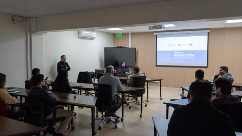 Una reunión en un aula con varias personas escuchando a un exponente.