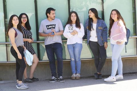 Un grupo de seis jóvenes posando juntos frente a una pared de vidrio.