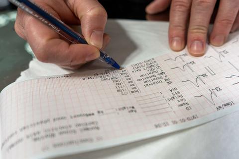 Una persona está tomando notas sobre un gráfico médico mientras escribe con un bolígrafo.