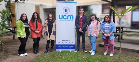 Un grupo de siete personas sonríe frente a un cartel de la UCM en un entorno al aire libre.