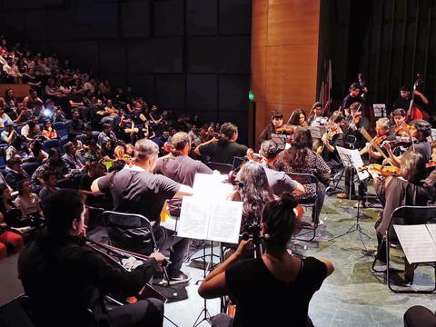 Concierto en un auditorio con una orquesta tocando frente a un gran público.