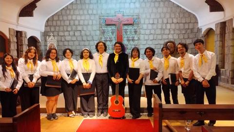 Grupo de jóvenes reunidos en una iglesia con guitarras y vestimenta formal.