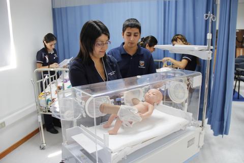 Una enfermera y un estudiante cuidan de un bebé en una incubadora en un entorno médico.