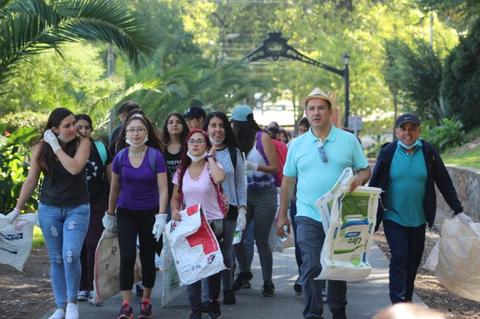 Un grupo de personas camina por un parque llevando bolsas, participando en una actividad comunitaria de limpieza.