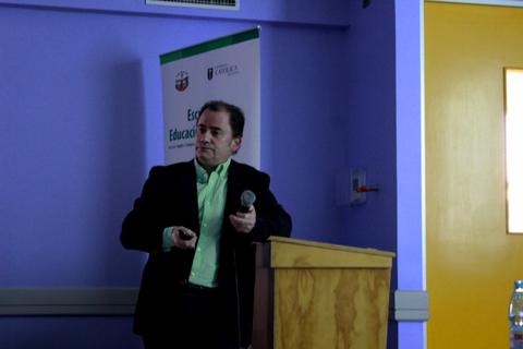 Un hombre presenta en un evento frente a una audiencia en un salón con paredes moradas.