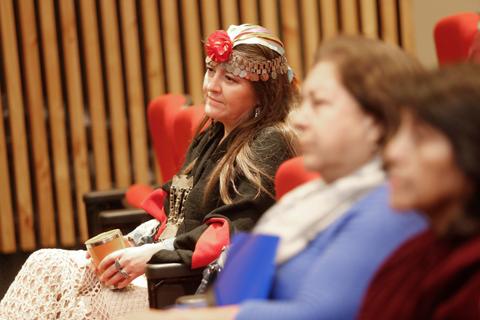 Mujeres sentadas en un evento, con una de ellas luciendo un atuendo tradicional y una diadema decorativa.