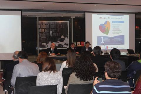 Una conferencia en un auditorio con varias personas sentadas y panelistas en el escenario.