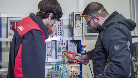 Dos técnicos trabajan en un panel eléctrico mientras realizan mediciones con un multímetro.