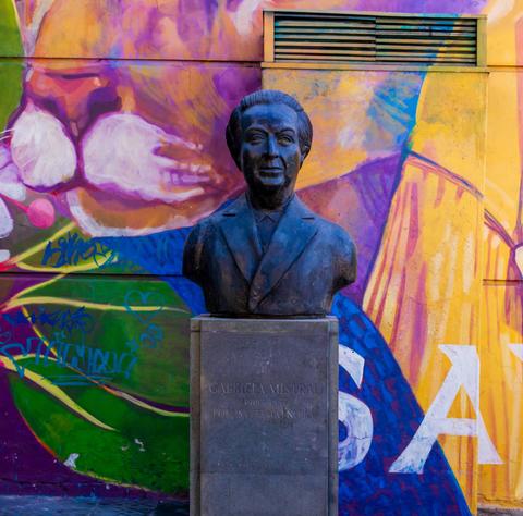 Una estatua de bronce de un destacado personaje chileno frente a un colorido mural.