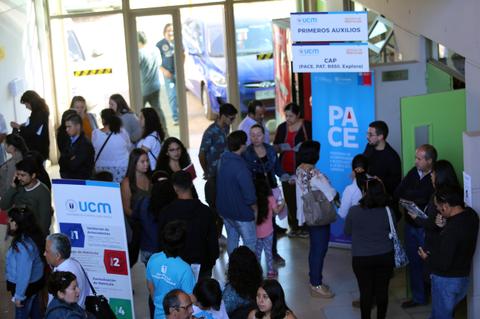 Una multitud de personas se reúne en un espacio interior, rodeadas de carteles y señalizaciones.