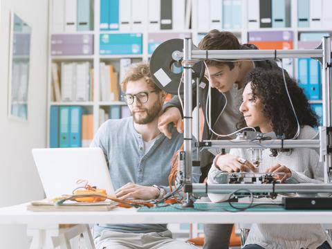 Tres personas trabajan juntas en un proyecto de impresión 3D en una oficina moderna.