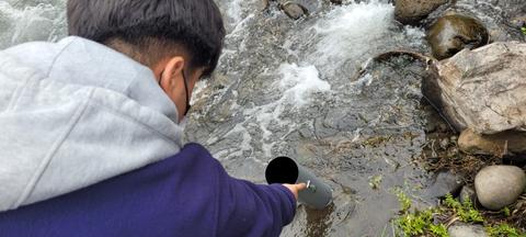 Una persona está tomando agua de un río con un tubo.