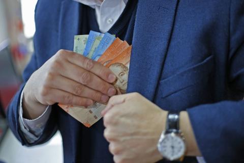 Una persona guarda billetes en el bolsillo de su chaqueta.