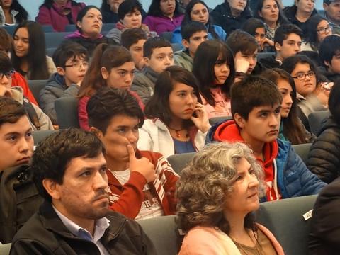 Un grupo de jóvenes y adultos observa atentamente un evento en un auditorio.