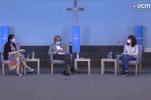Tres personas sentadas en un panel de discusión, con mascarillas, en un ambiente académico.